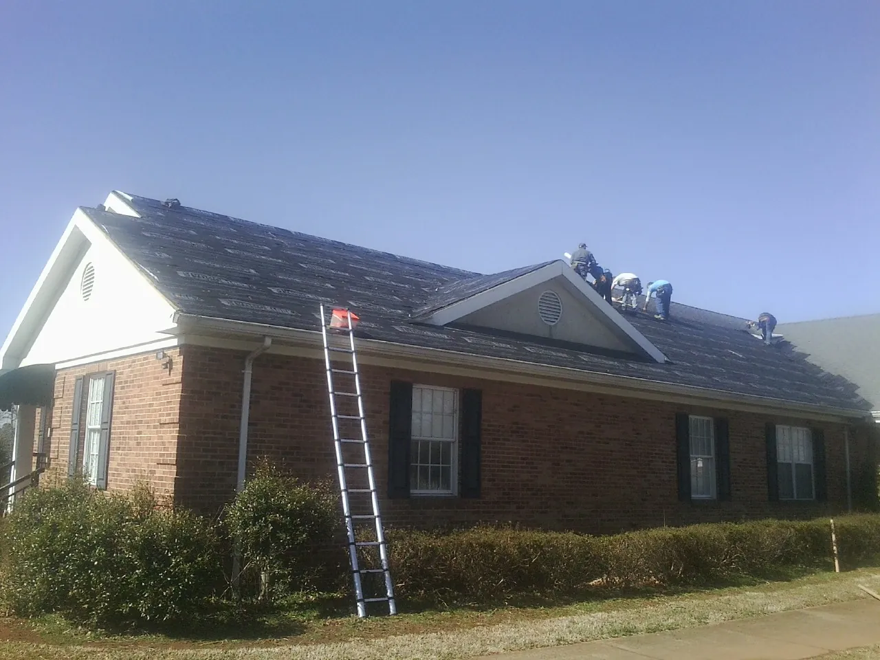 Crew tearing shingles off a brick ranch roof with a ladder set — Metal Roof Repair work by our crew in Northfield